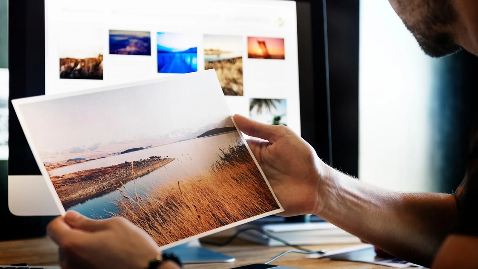 Ausgedrucktes Foto wird vor einem Bildschirm mit Bildern betrachtet