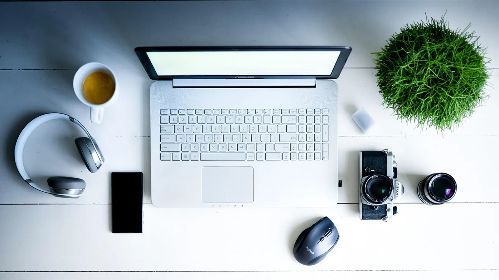 Arbeitsplatz mit Laptop, Kamera, Objektiv und Kopfhörern von oben